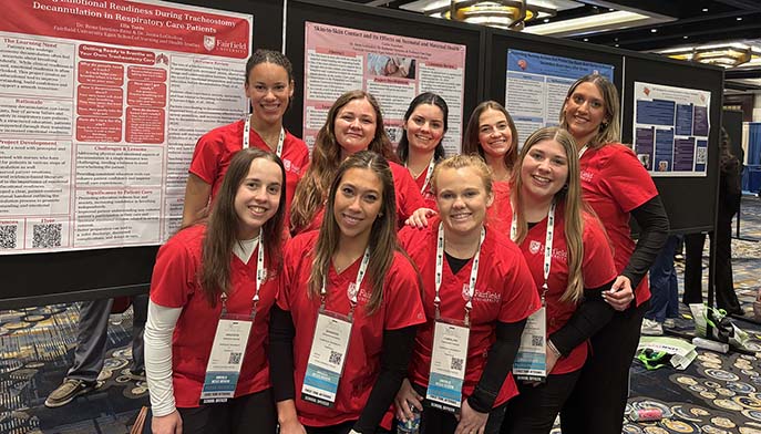A group of young women in red shirts stands beside a colorful poster, smiling and engaging with each other.