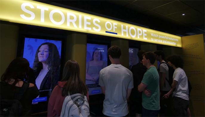 People are gathered in front of a large display showing the phrase "Stories of Hope."
