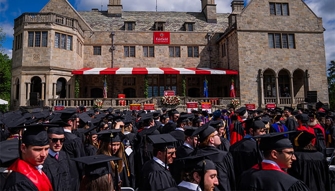 Students in caps and gowns lined up at their seats on a bright, sunny day as Commencement exercises begin.