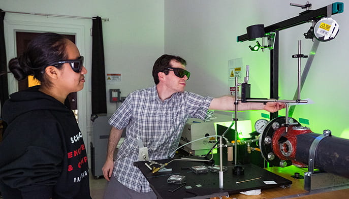 Engineering student and mentor wearing protective eyegear as they conduct experiments with a green, laser-based optical flow diagnostic system.