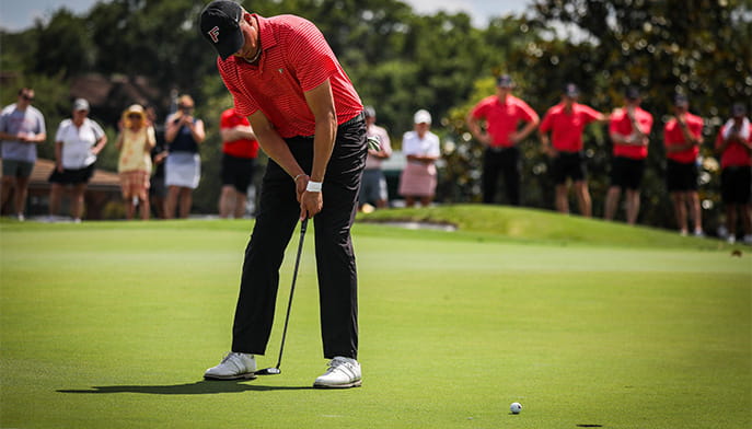 Sophomore golfer lining up a putt shot in front of supportive teammates and fans.