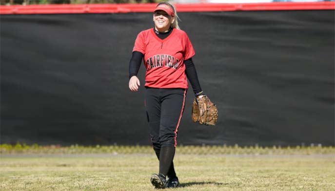 A female softball player wearing a red and black uniform, ready to pitch on the field.