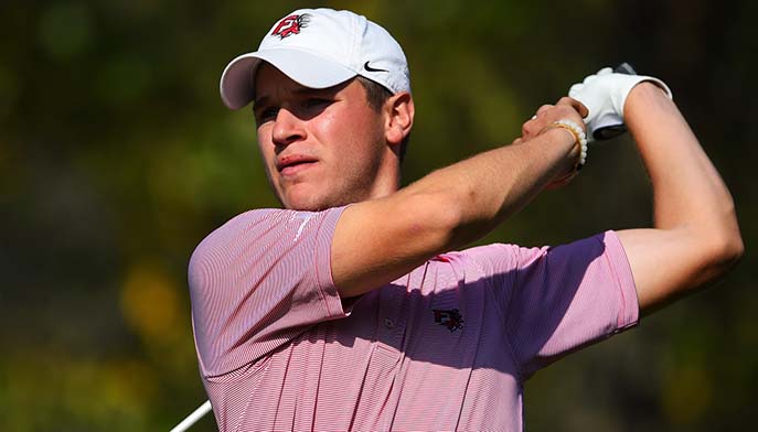 A man wearing a red shirt and white hat takes a swing with his golf club on the course.