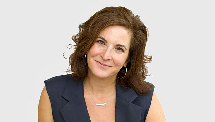 Michelle Farrell, PhD, with shoulder-length brown hair smiles gently, wearing a dark sleeveless top and hoop earrings. The background is plain light grey, conveying a professional yet approachable tone.