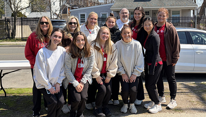 A group of thirteen people, pose together outdoors. They are smiling and wearing casual and matching team attire, conveying a sense of unity and joy.