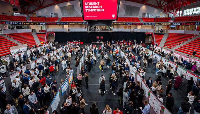 Wide view of a bustling Student Research Symposium at the Leo D. Mahoney Arena. Attendees study posters on display, creating an energetic and collaborative atmosphere.