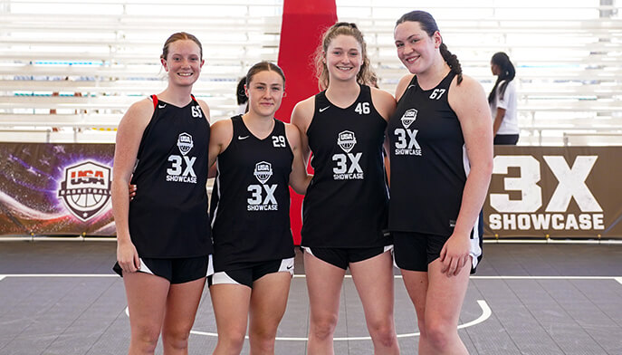 Four smiling young women in matching black basketball jerseys stand on an indoor court with "3X Showcase" branding in the background.