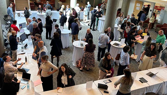 Overhead view of a busy indoor networking event, with people gathered around tables and white cocktail roundtables in a lobby.