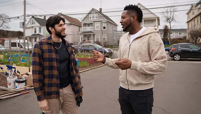 Two men engaged in conversation on a residential street, surrounded by houses.