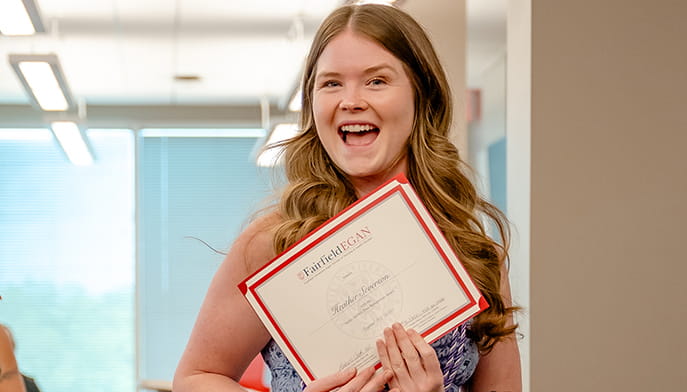 Severson smiles proudly while holding a certificate in her hands, celebrating her achievement.
