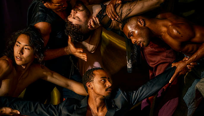 Dancers of various skin tones overlap and twist their bodies, joining hands or placing them on others’ arms, wrists, heads.