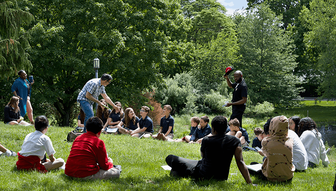 Writing workshop students participating in a group activity while sitting outside on a bright, sunny day.