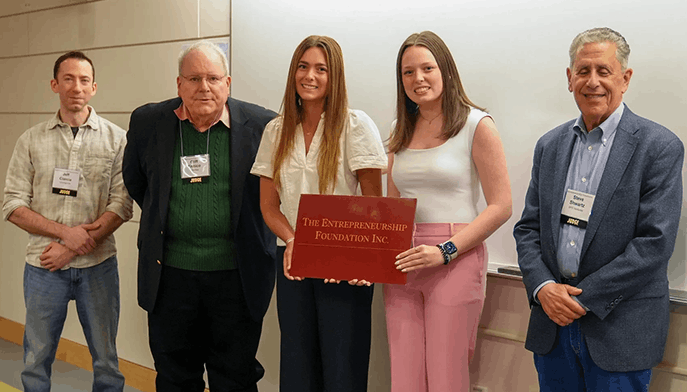 Members of the two-woman StartUp team, MiniMinds, holding a 'The Entrepreneurship Foundation Inc.' sign with the CT Collegiate Business judges.