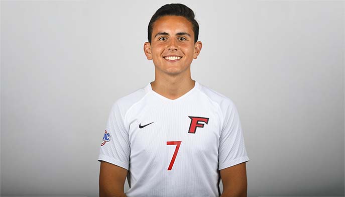 Smiling Fernando Robayo ’21 poses in a white jersey with a red “F” logo and number 7 against a neutral gray studio background.
