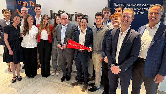 Fairfield Dolan faculty and students smiling at an event, gathered around a red ribbon, with a branded backdrop and an upbeat, celebratory mood.
