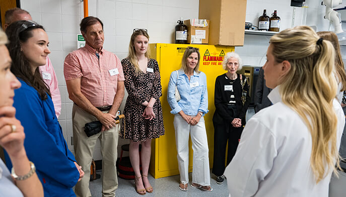 Researchers in white lab coats discuss a scientific poster on noncanonical peptides in a laboratory, creating an informative, collaborative mood.