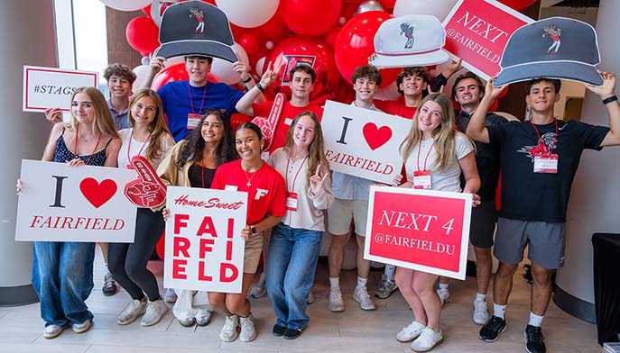 A group of people joyfully holding signs that say "I Love Fairfield" in a vibrant outdoor setting.