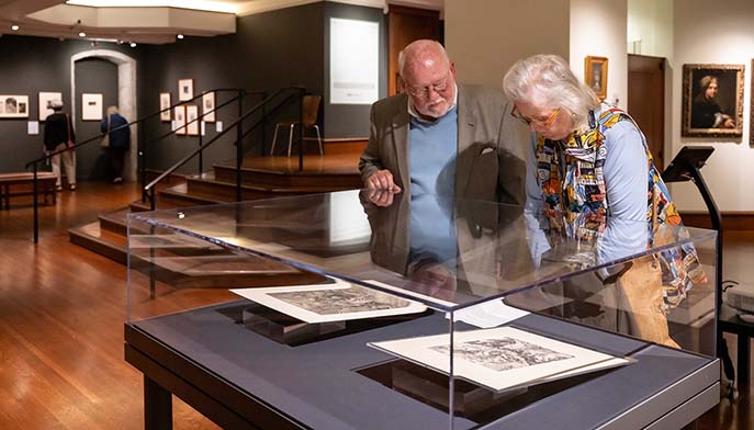 Two visitors admire a colorful painting in a museum, engaged in conversation about the artwork.