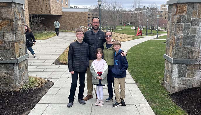 A happy family stands together in front of a charming stone building, smiling for the camera.
