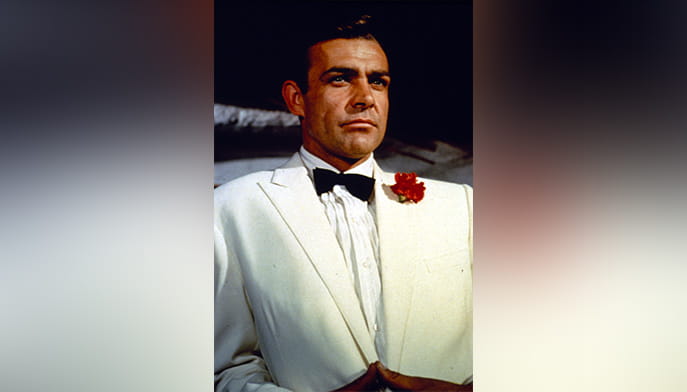 Sean Connery as James Bond in a white tuxedo with black bow tie and red boutonnière, projecting a poised, confident, serious demeanor.