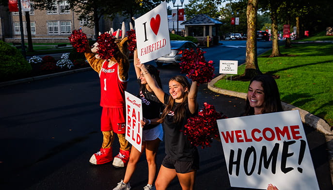 New student leaders and Lucas the Stag holding up pom-poms and various welcoming signs at move-in, such as 'Welcome Home!' and 'I [heart] Fairfield'.