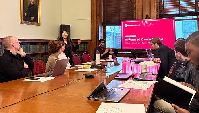A meeting on AI-powered knowledge features attendees around a conference table, with laptops, a presenter, and a bright red slide on screen.