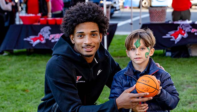A man and a young boy stand together, each holding a basketball, smiling at the camera.