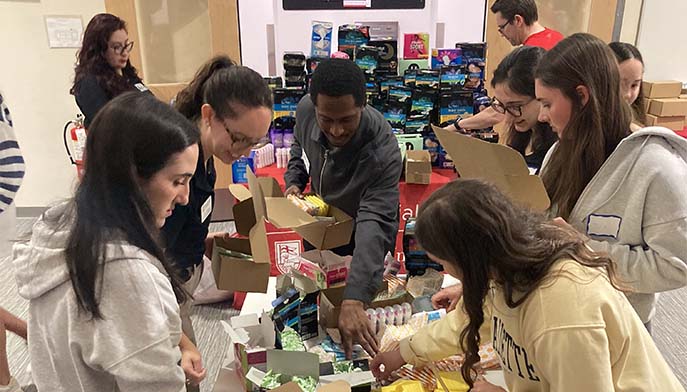 Image of members from the AOCN, CSI, Campus Ministry, and Fairfield Bellarmine communities, organizing feminine hygiene products into boxes