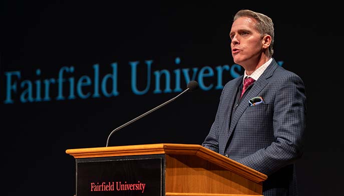 A well-dressed man delivering a speech, standing confidently at a microphone.