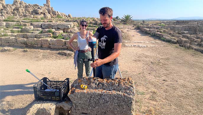 Image of a man and woman standing side by side next to a large stone block outdoors.