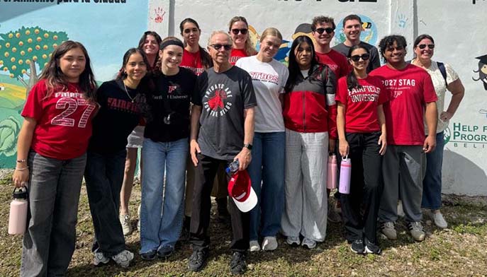 A group of people stands together outdoors in front of a painted wall, many wearing red and Fairfield University apparel, posing and smiling at the camera.