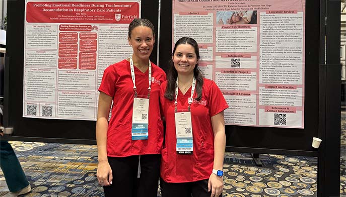 Two conference presenters in red shirts stand in front of a research poster display.