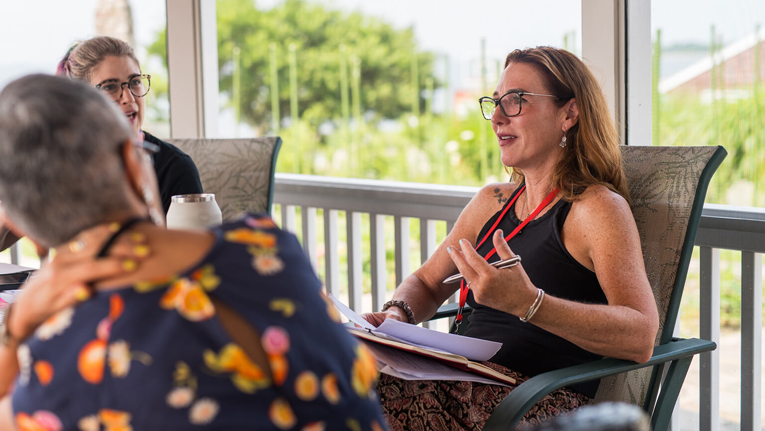 Two women engage in conversation on a porch, enjoying each other's company in a relaxed outdoor setting.