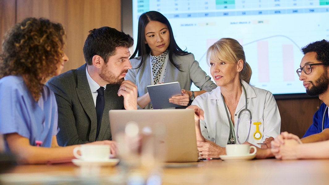 Working healthcare professionals sitting in a conference room going over trends, stats, and data.