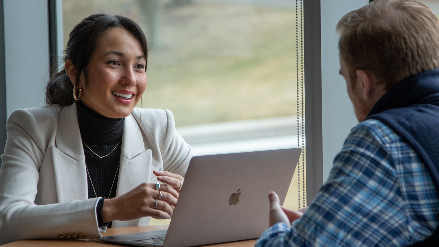 Three young adults, two men and one woman, walk together outside a building. They wear business casual attire and appear engaged in conversation, smiling.