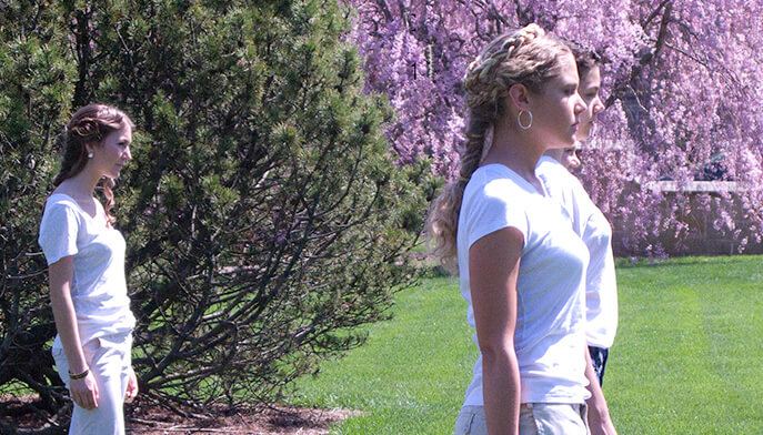 A woman is positioned in a grassy area, gazing ahead with a serene expression, surrounded by nature.
