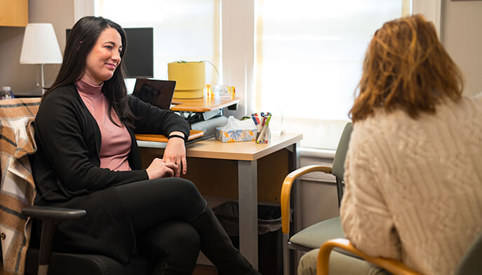 A woman talks while seated in a chair, interacting with another woman beside her.