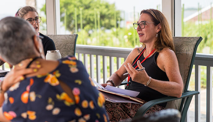 Two women engage in conversation on a porch, enjoying each other's company in a relaxed outdoor setting.