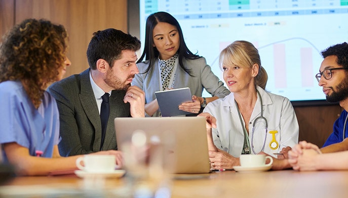 Working healthcare professionals sitting in a conference room going over trends, stats, and data.