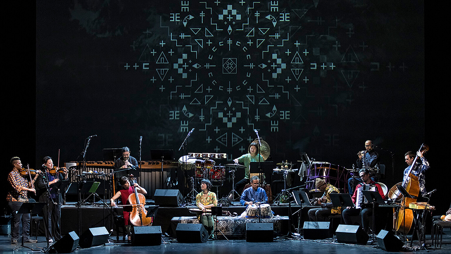 Musicians play on stage, accompanied by a large screen showcasing dynamic visuals in the background.  