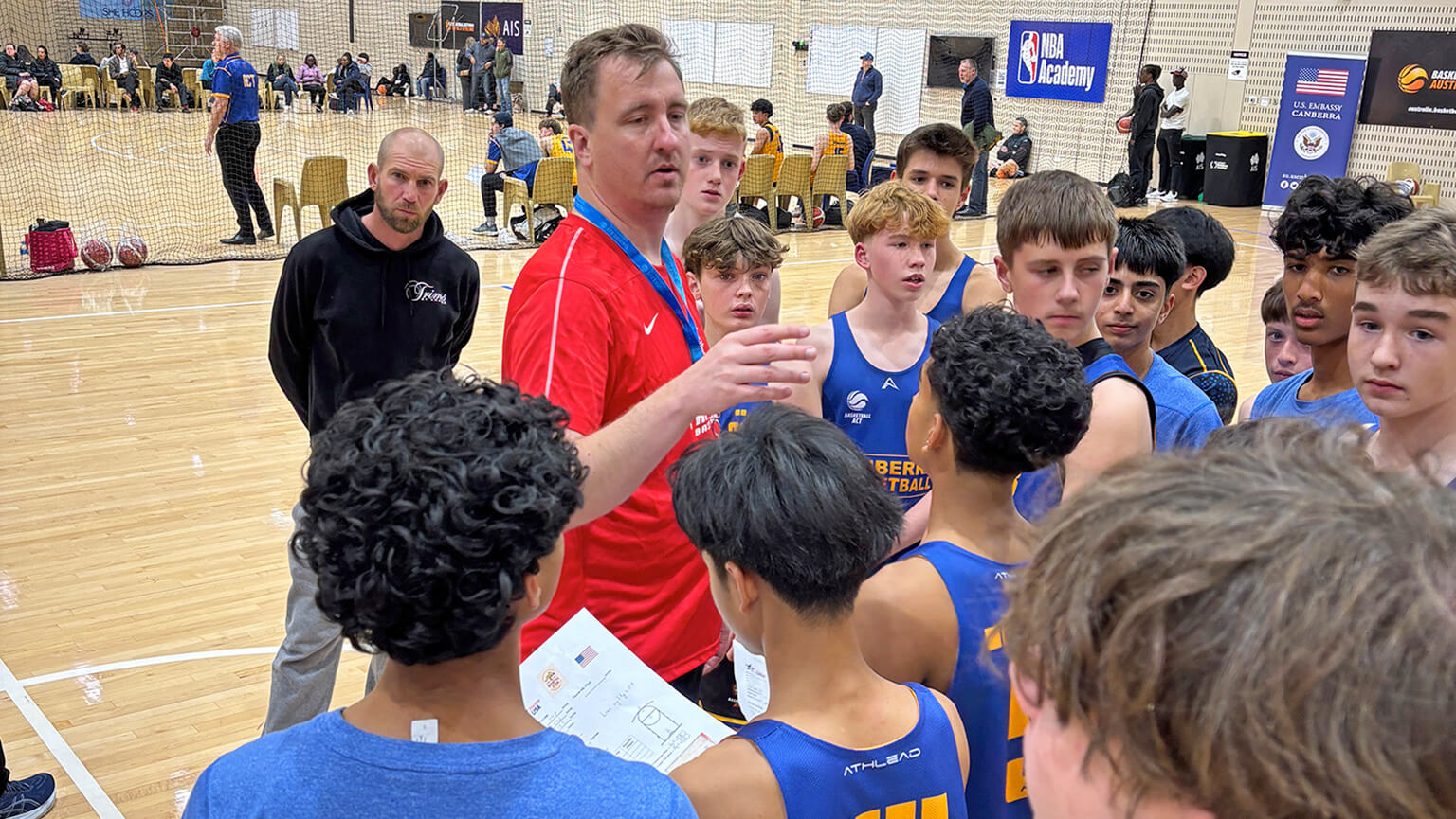 A group of boys is positioned around a basketball court, interacting and preparing for a game or practice.