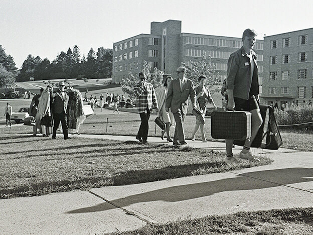 Several individuals strolling down a sidewalk on Fairfield Campus in 1966, engaged in conversation and enjoying the outdoors at move-in day.