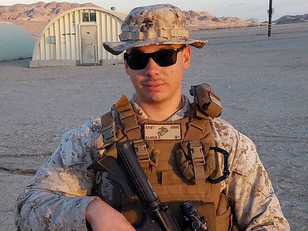 A soldier in military attire holds a rifle while standing in a barren desert landscape under a clear sky.