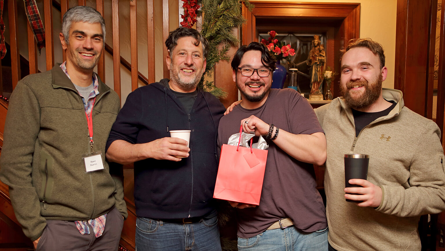 A group of four men poses together, showcasing a red bag in a friendly photograph.