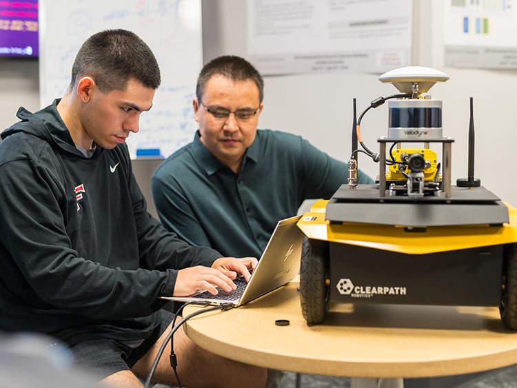 Engineering student and professor working together on programming a Jackal unmanned ground vehicle (UGV).