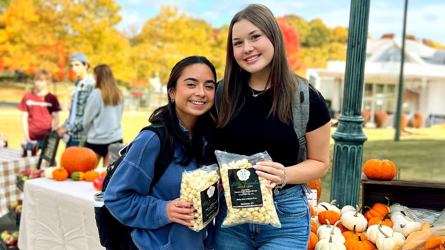 Two female students enjoying popcorn together on campus, surrounded by lively activity.