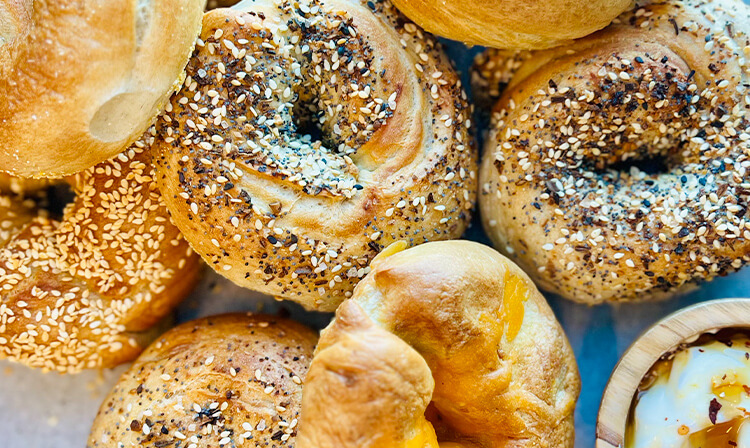 A detailed view of sesame seed bagels accompanied by a small bowl of dip, highlighting their texture and color.