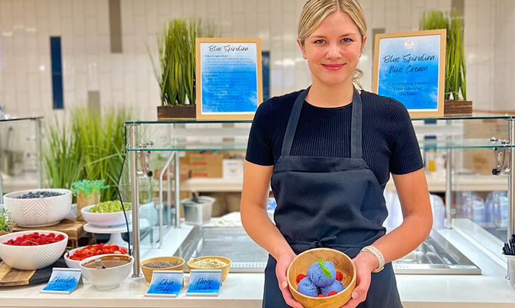 A woman wearing an apron holds a bowl of fresh fruit, showcasing her culinary enthusiasm.  