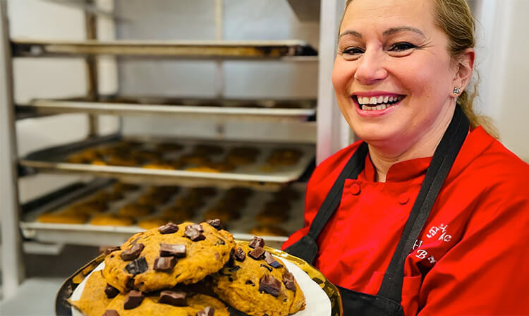 A woman in a red shirt holds a tray filled with freshly baked chocolate chip cookies.