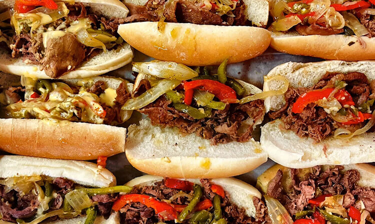 A tray filled with beef and pepper sandwiches, showcasing a variety of colorful toppings and fresh bread.